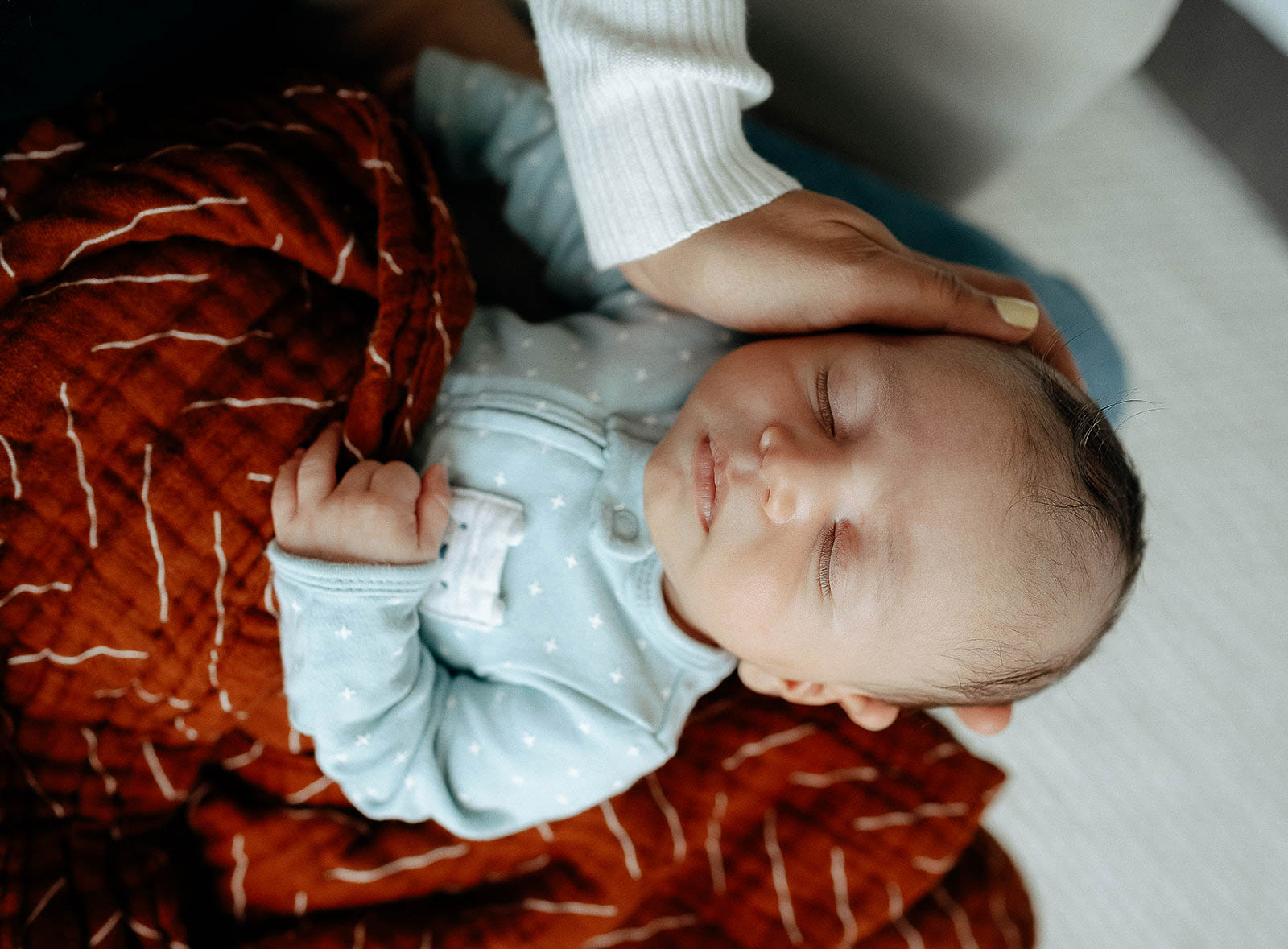 Sleeping newborn wrapped in a rust color blanket.