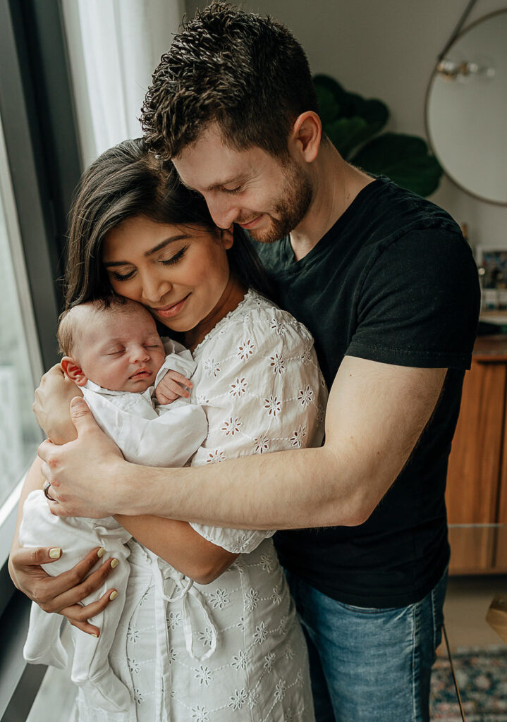 NYC in home family newborn session, family of three. Mom hd her newborn son and dad hugging his family