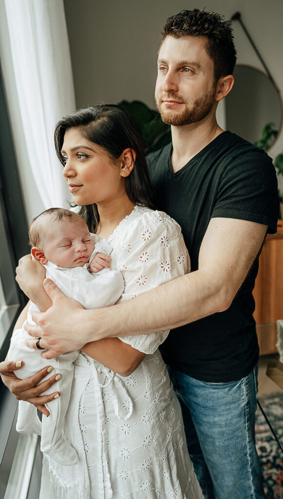 In home newborn session in New York City family of three mom holding baby and dad holding mom.