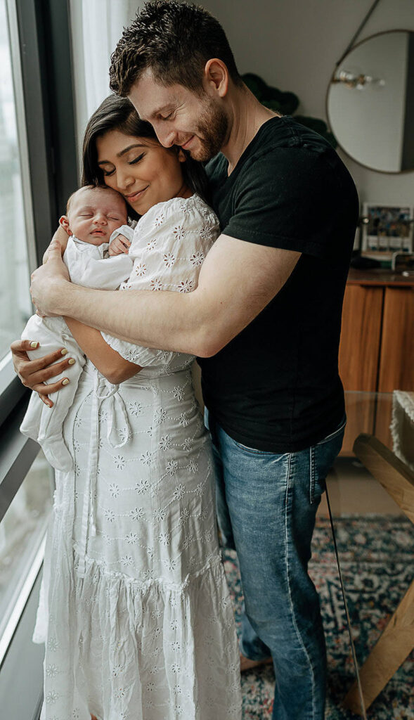 NYC in home family newborn session, family of three. Mom holding her newborn son and dad hugging his family. 