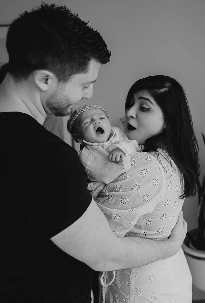 black and white photo of mom and dad holding their newborn son while he is yawning.